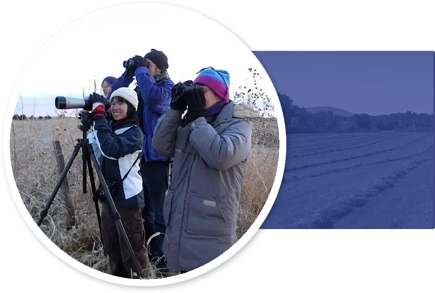 Group of people wearing winter coats and hats in a field with binoculars birdwatching