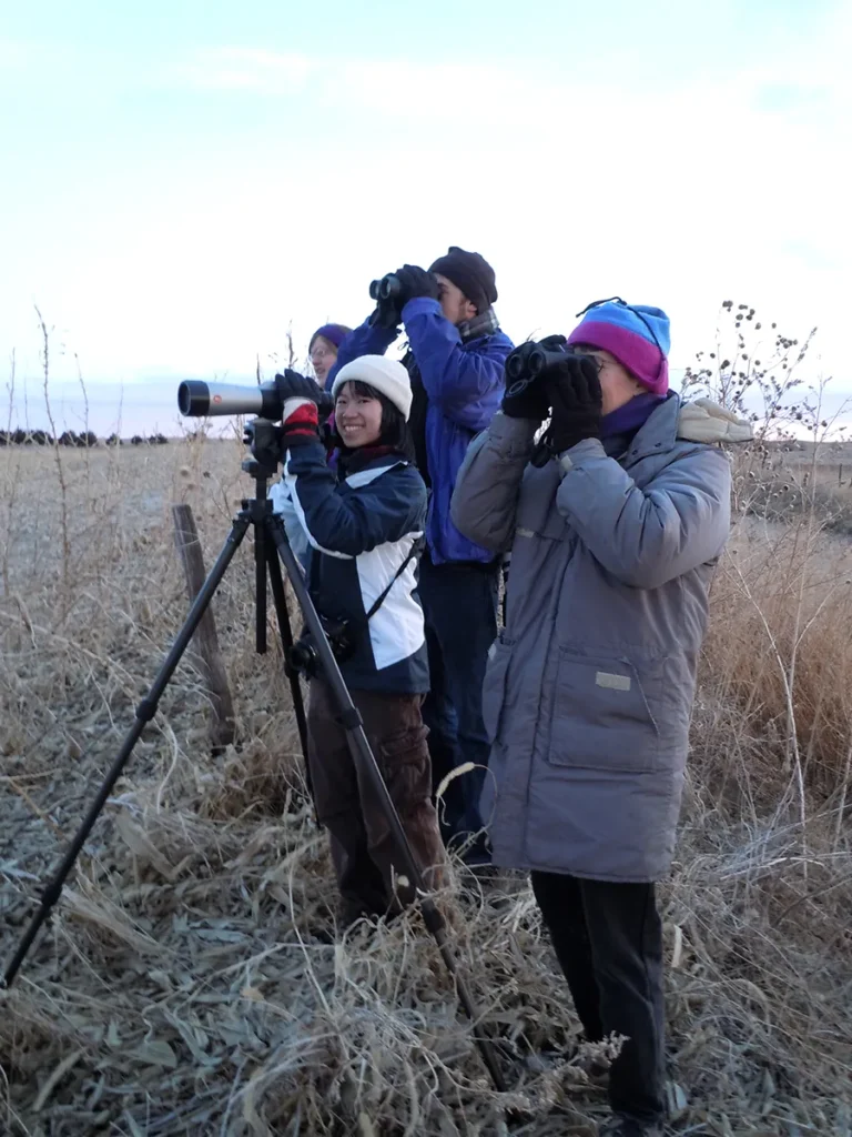 Group of people wearing winter coats and hats looking through binoculars birdwatching